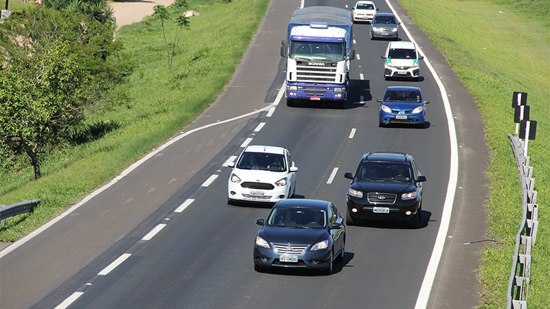 Foto de carros e um caminhão rodando na estrada.