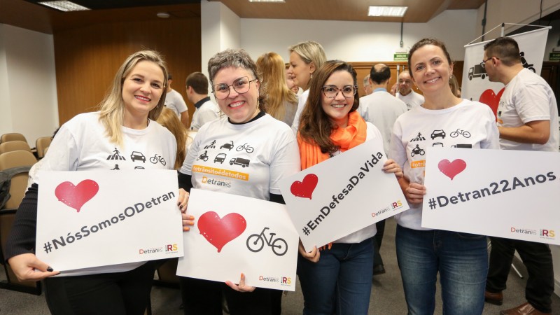 Servidoras do DetranRS seguram cartazes com as mensagns: #nossomosodetran, Eu amo bicicleta, #emdefesadavida e #Detran22anos