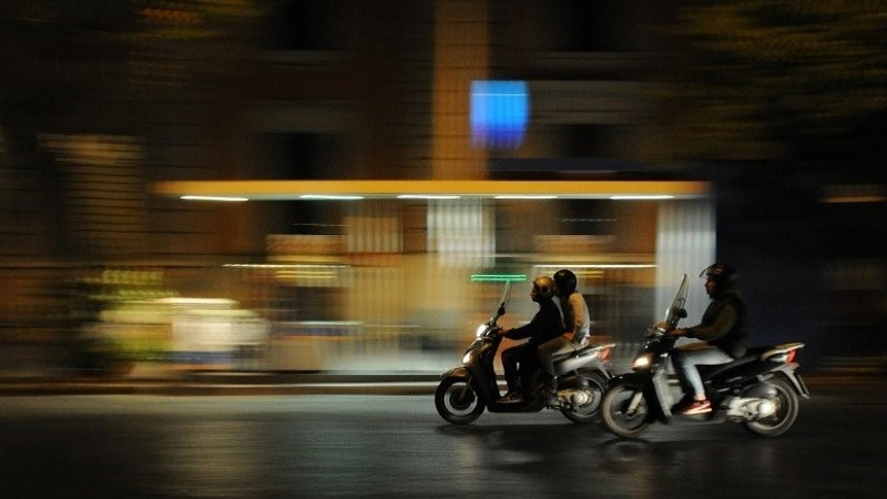 Foto mostra motociclistas trafegando em uma via urbana