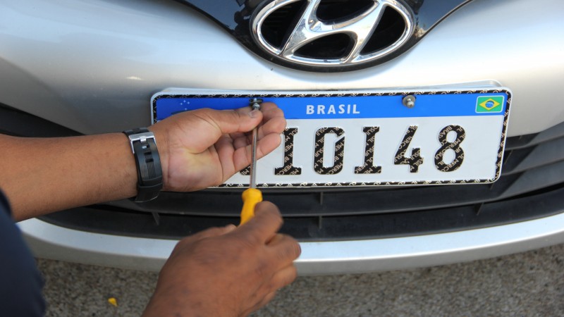 Mãos instalando uma placa padrão Mercosul em um veículo de cor prata