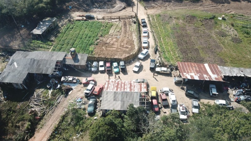 Imagem aérea do pátio de um desmanche que mostra veículos estacionados e pavilhões, capturada durante o dia