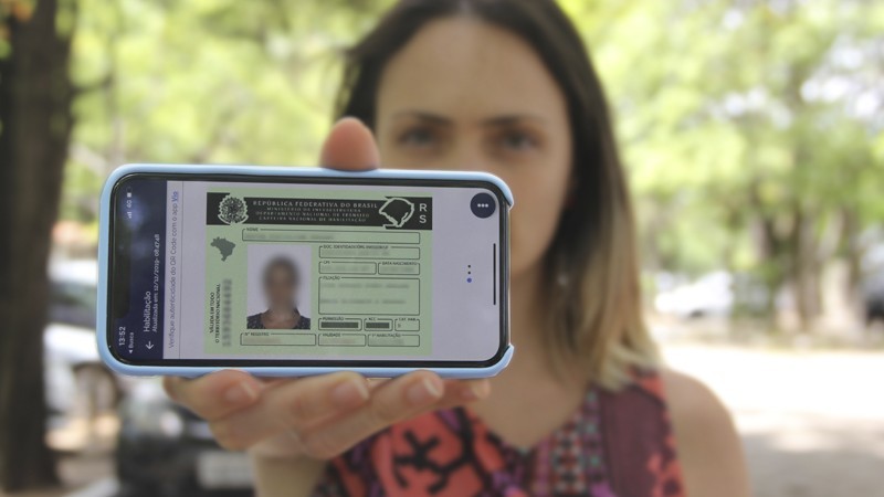 A imagem mostra uma mulher segurando o celular à sua frente, com o documento CNH digital aparecendo em primeiro plano