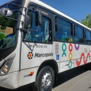 Visto de lado, um ônibus branco com a identidade visual da Escola Pública de Trânsito e cílios nos farois