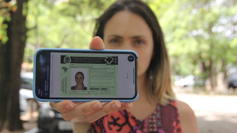 Mulher aponta para camera um celular com a CNH digital na tela