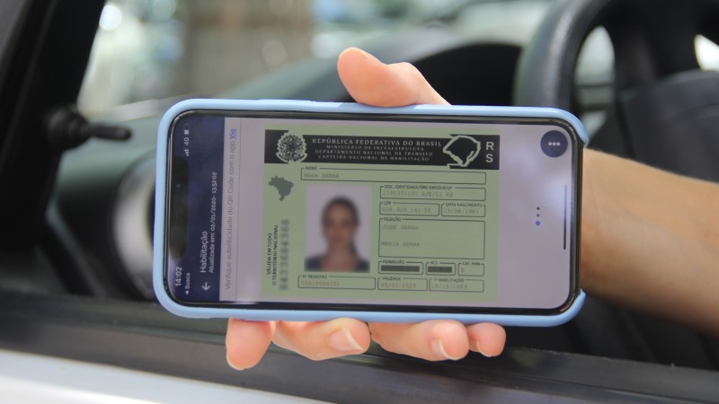 Da janela de um carro, braço de motorista aponta celular para a câmera com CNH digital
