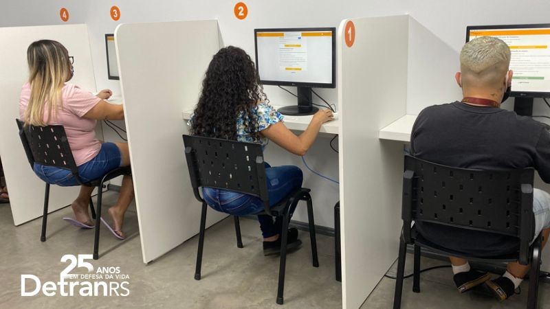 Candidatos a Carteira Nacional de Habilitação sentados de costas em cabines fazendo a prova teórica em um computador