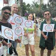 Foto diurna que mostra os servidores do DetranRS e alguns jovens abordados na ação educativa, em pé, posicionados lado a lado e segurando plaquinhas com mensagens educativas de trânsito