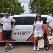 Servidores do DetranRS sorridentes, parados em frente à viatura do órgão