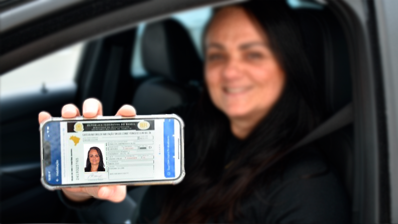 Condutora sorrindo e apresentando sua CNH na versão digital em seu celular
