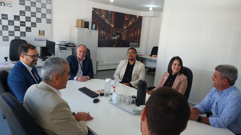 Foto horizontal colorida mostra seis homens e uma mulher sentados em uma mesa de reunião