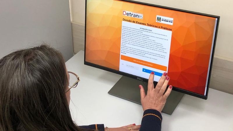 Foto horizontal colorida mostra mulher de óculos em frente a um computador tocando na tela