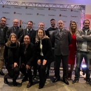 Foto horizontal colorida mostr grupo de treze homens e mulheres em frente ao backdrop do Detran
