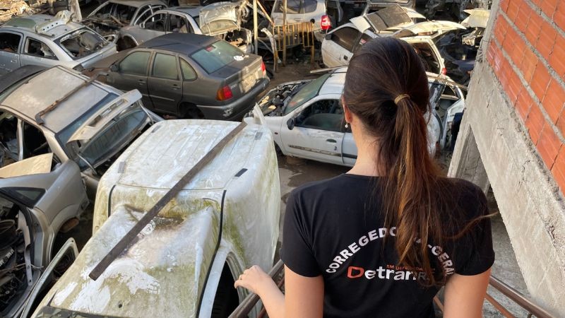 Servidora da Corregedoria do Detran, de constas, chegando no pátio do desmanche, onde há vários veículos e sucatas armazenados