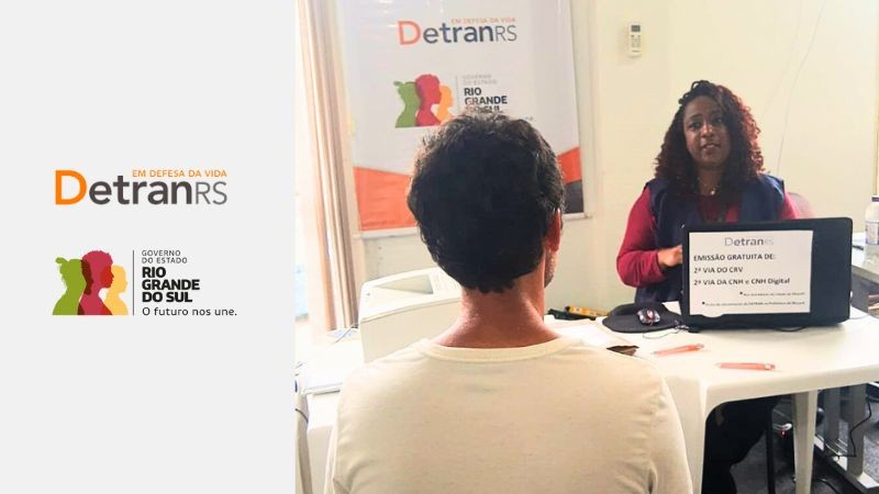 Foto colorida mostra atendente mulher sentada em frente a um notebook falando com um homem que aparece de costas. Ao fundo, um banner com as logos do DetranRS e Governo do RS