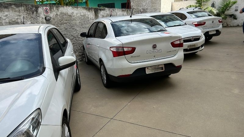 Foto horizontal colorida mostra quatro carros brancos estacionados em um pátio