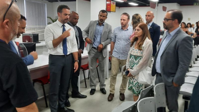 Foto horizontal colorida mostra grupo de homens em pé na nova unidade do Tudo Fácil olhando para o governador falando