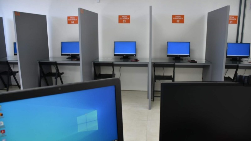 Foto horizontal colorida mostra sala separada em guichês com monitores de computador