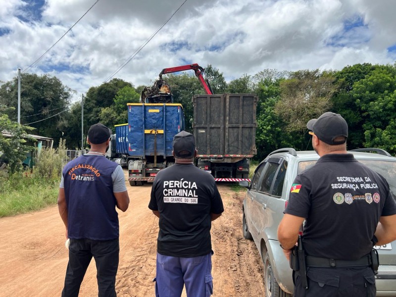 Foto mostra três servidores da SSP, do DetranRS e do IGP de costas. Eles olham para caminhão-garra que suspende sucata veicular.