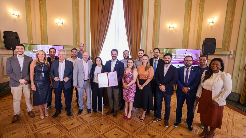 Foto horizontal colorida mostra grupo de pessoas posando para foto. No centro, o governador Eduardo Leite mostra uma pasta com documentos assunados