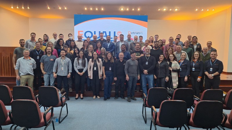 Foto horizontal colorida mostra grupo de pessoas em frente ao palco de um auditório posando para a foto