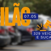 Card com foto embaçada ao fundo de veículos estacionados lado a lado. Em frente, no canto superior esquerdo em laranja está escrito leilão e em azul com fonte branca a data de 07.05. No lado direito um martelo laranja e abaixo em azul com fonte em branco 329 veículos e sucatas.