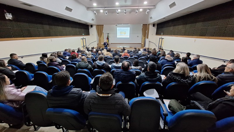 Foto horizontal colorida mostra pessoas de costas em um auditório lotado