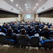 Foto horizontal colorida mostra pessoas de costas em um auditório lotado